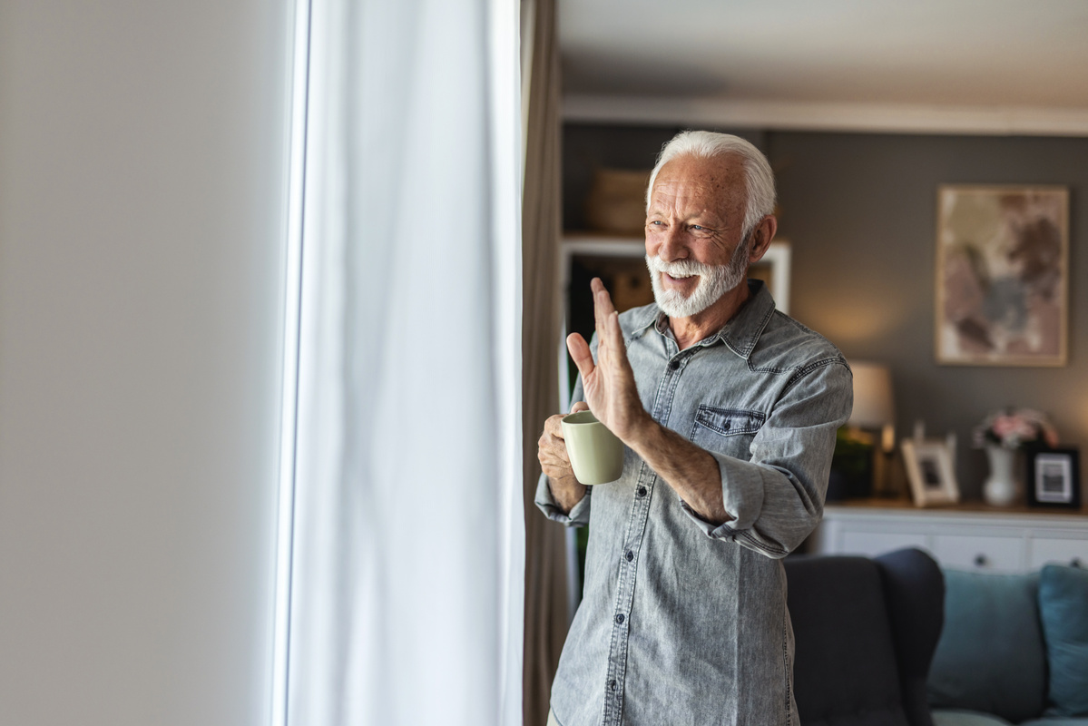 Älterer Mann winkt am Fenster